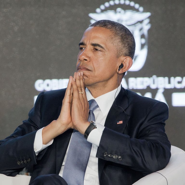 Barack Obama faltet die Hände vor dem Gesicht zusammen, während er auf einer Konferenz einen Kopfhörer im Ohr hat. (Foto: picture-alliance / Reportdienste, Pablo Martinez Monsivais)