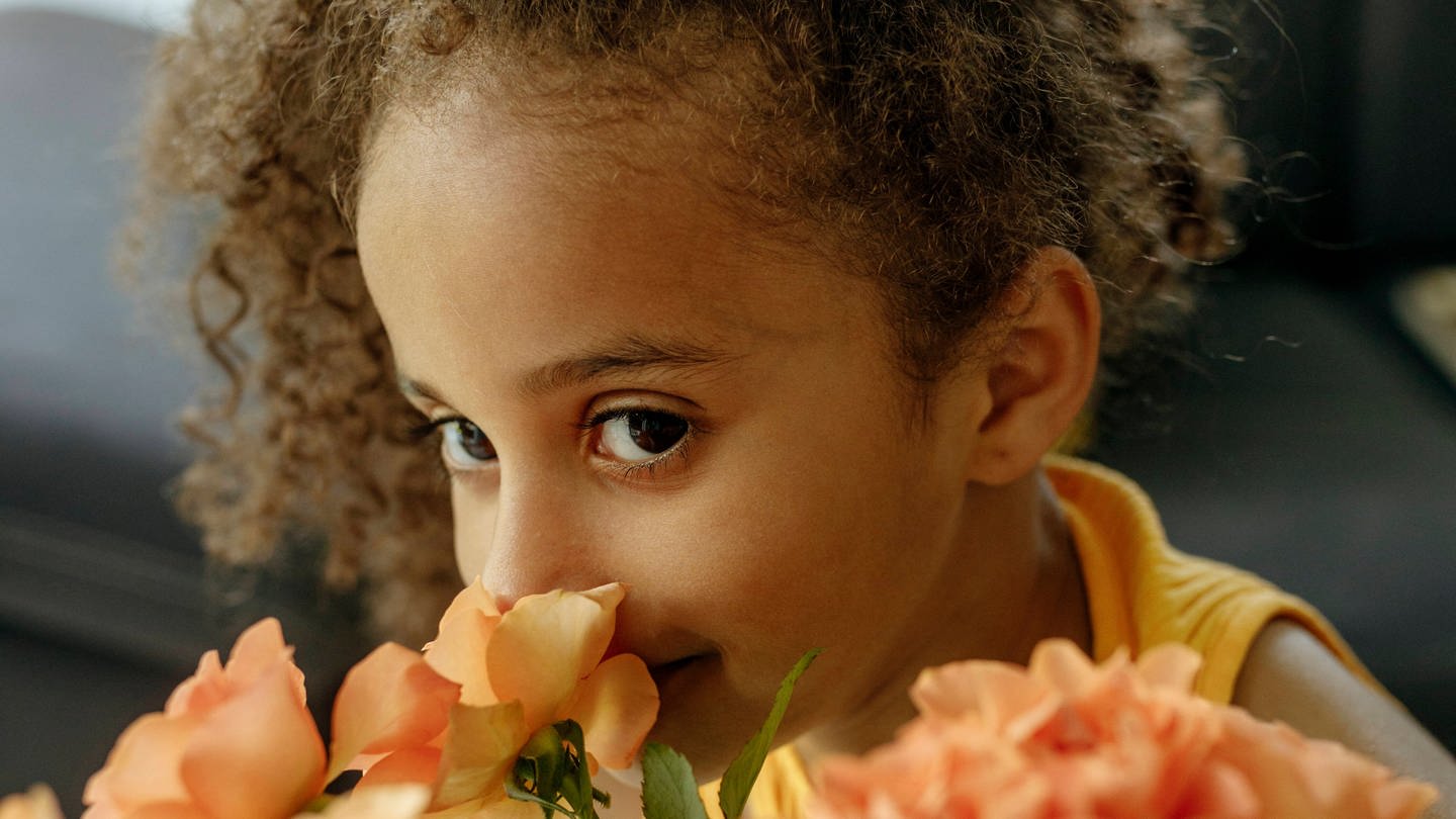 Ein junges Mädchen riecht an rosen (Foto: IMAGO, IMAGO / Westend61)
