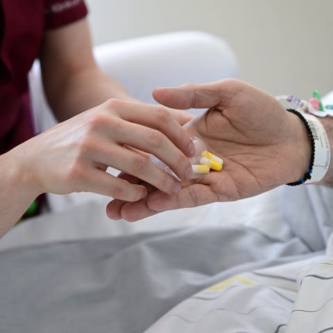 Symbolbild: Eine Pflegerin gibt einem Patienten Tabletten. (Foto: picture-alliance / Reportdienste, picture alliance/dpa | Bernd Weißbrod)