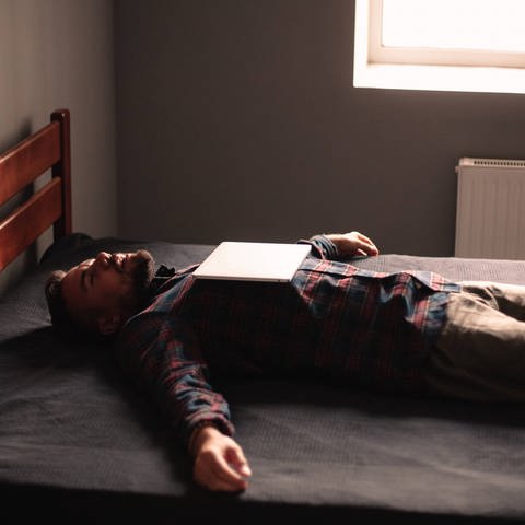 Ein Mann liegt erschöpft im Bett (Foto: IMAGO, IMAGO / Cavan Images)