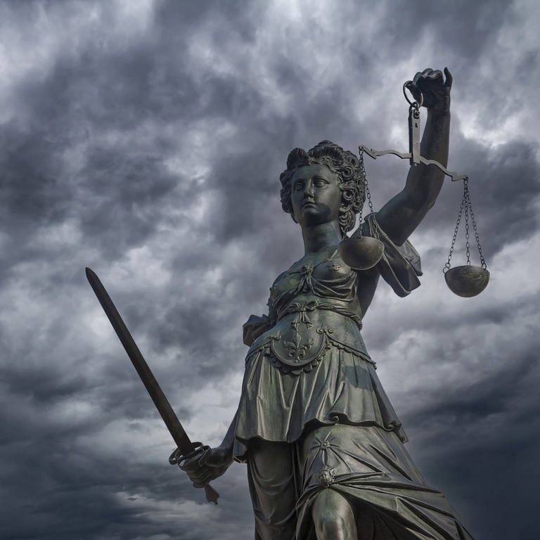 Justitia am Gerechtigskeitsbrunnen am Römerberg in Frankfurt  Main vor dunklen Regenwolken: In Deutschland gibt es Fehlurteile. Die Hürden für die Wiederaufnahme eines abgeschlossenen Strafverfahrens sind jedoch sehr hoch gesetzt. 