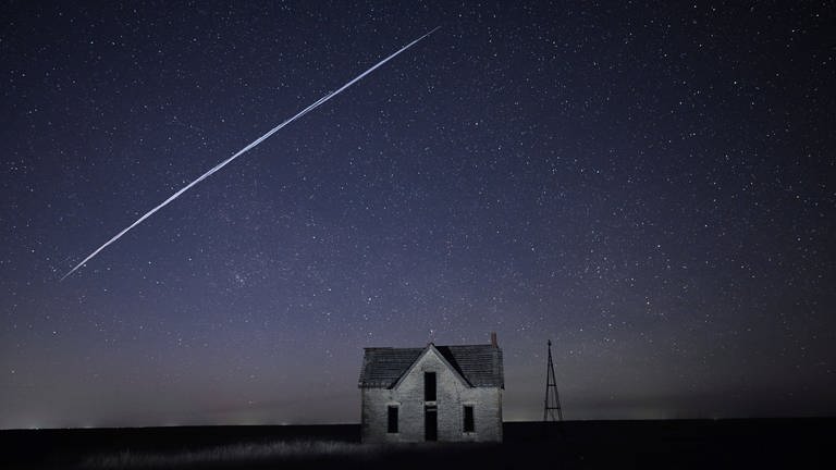 Auf diesem Foto, das am 6. Mai 2021 mit Langzeitbelichtung aufgenommen wurde, fliegt eine Reihe von Starlink-Satelliten über ein altes Steinhaus in der Nähe von Florence, Kansas