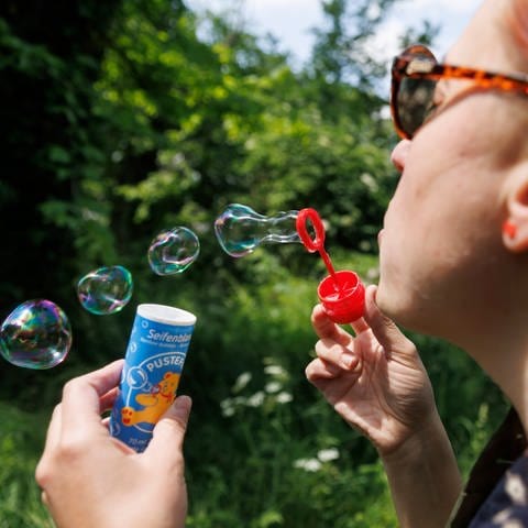 Eine Frau bläst Seifenblasen mit einem Spielzeug der Marke Pustefix.
