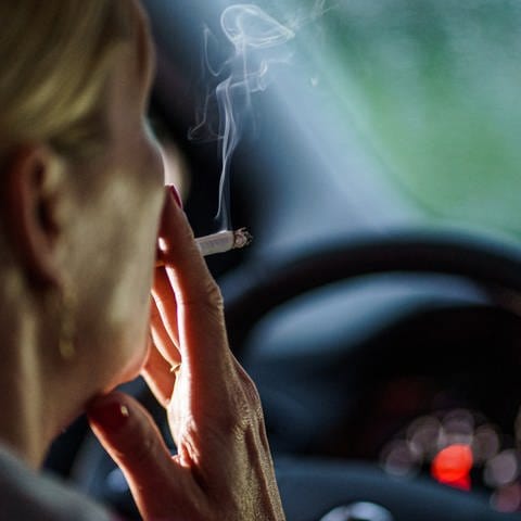 Eine Frau zieht hinter dem Lenkrad ihres Autos an einer Zigarette.