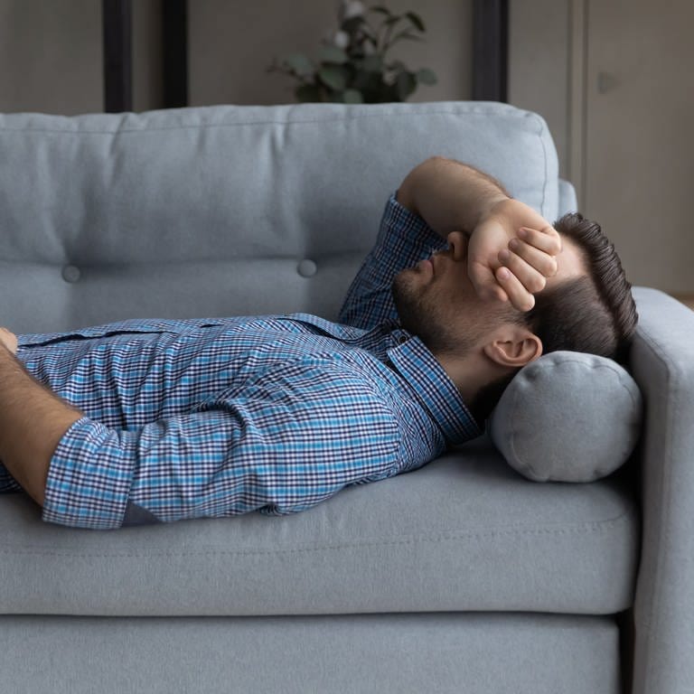 Symbolbild: Ein erschöpfter Mann liegt auf der Couch (Foto: IMAGO, IMAGO / Pond5)