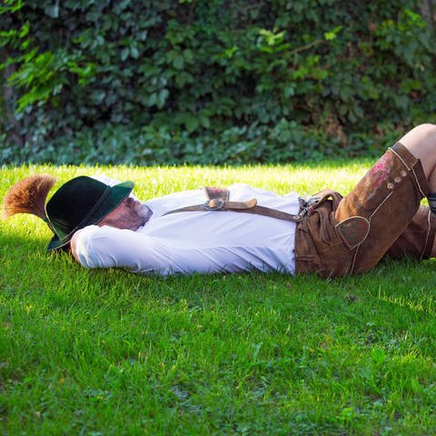 Mann in bayerischen kleidung schläft draußen im Gras 