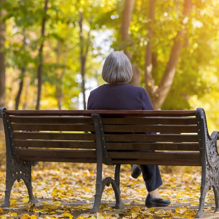 Ältere Frau sitz in einem Herbstwald einsam auf einer Bank: Einsamkeit ist ein wachsendes gesellschaftliches Problem. Unterschiedliche Projekte sollen einsamen Menschen helfen