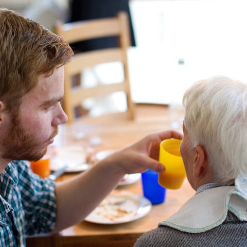 Junger Mann hilft einer älteren Frau beim Einnehmen einer Mahlzeit.