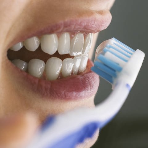 Eine Frau putzt sich die Zähne mit einer Handzahnbürste.
