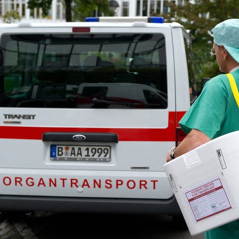 Ein Mann bringt einen Behälter zum Transport von zur Transplantation vorgesehenen Organen, zu einem Fahrzeug für den Organtransport.