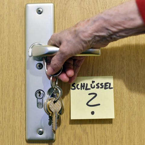 Symbolbild für die Alzheimer Erkrankung: ein Klebezettel mit dem Schriftzug "Schlüssel" klebt an einer Tür neben der Türklinke, an der ein Schlüsselbund hängt.