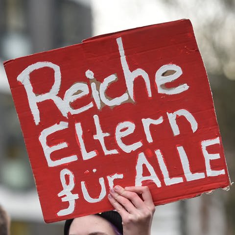 Jemand hält ein Plakat mit dem Slogan "Reiche Eltern für Alle" hoch.  (Foto: picture-alliance / Reportdienste, picture alliance/dpa | Uwe Zucchi)