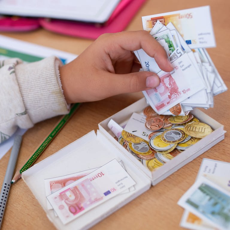 Das Wissen von Kindern und Jugendlichen über Finanzen ist dünn und sie wünschen sich selbst bessere Aufklärung: Eine Schülerin einer 2. Klasse rechnet im Klassenzimmer einer Grundschule mit Spielgeld