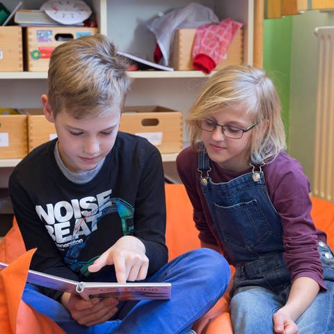 Zwei Schüler in der Grundschule lesen zusammen ein Buch und sitzen auf einem Sitzsack