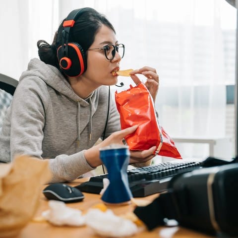Eine junge Gamerin starrt auf den Monitorbildschirm und isst Chips.
