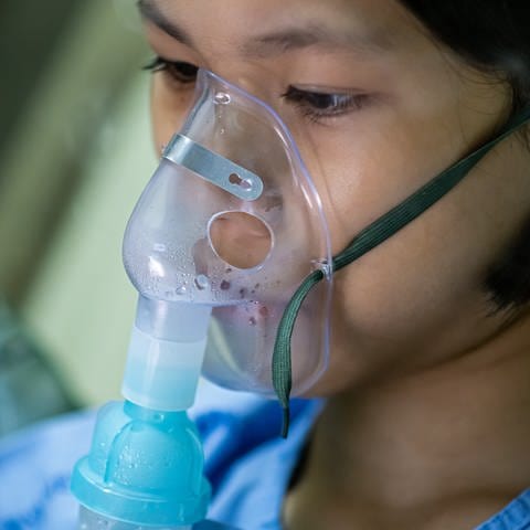 Nahaufnahme eines kranken asiatischen Mädchens mit Sauerstoffmaske im Gesicht, auf dem Bett im Krankenhaus