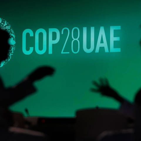 Zwei Menschen unterhalten sich vor einem Logo des UN-Klimagipfels COP28. 