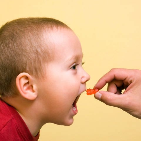 Ein kleiner Junge bekommt ein Gummibärchen in Mund gesteckt.