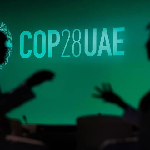 Zwei Menschen unterhalten sich vor einem Logo des UN-Klimagipfels COP28