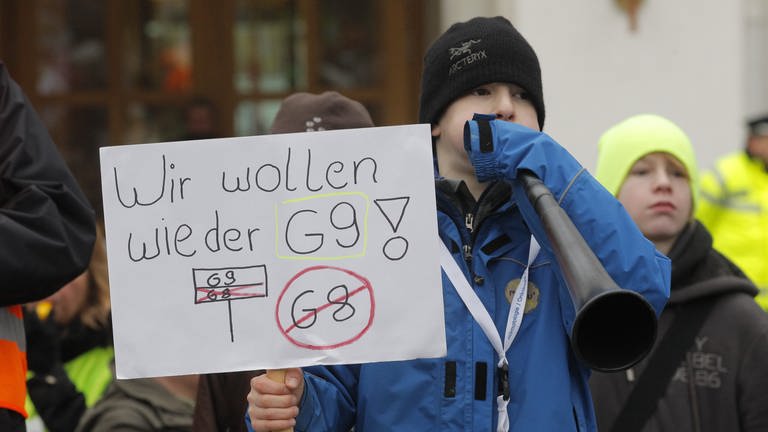 Demonstration für das neunjährige Gymnasium. Ein Junge mit einer Tafel in der Hand und der Aufschrift "Wir wollen wieder G9". 