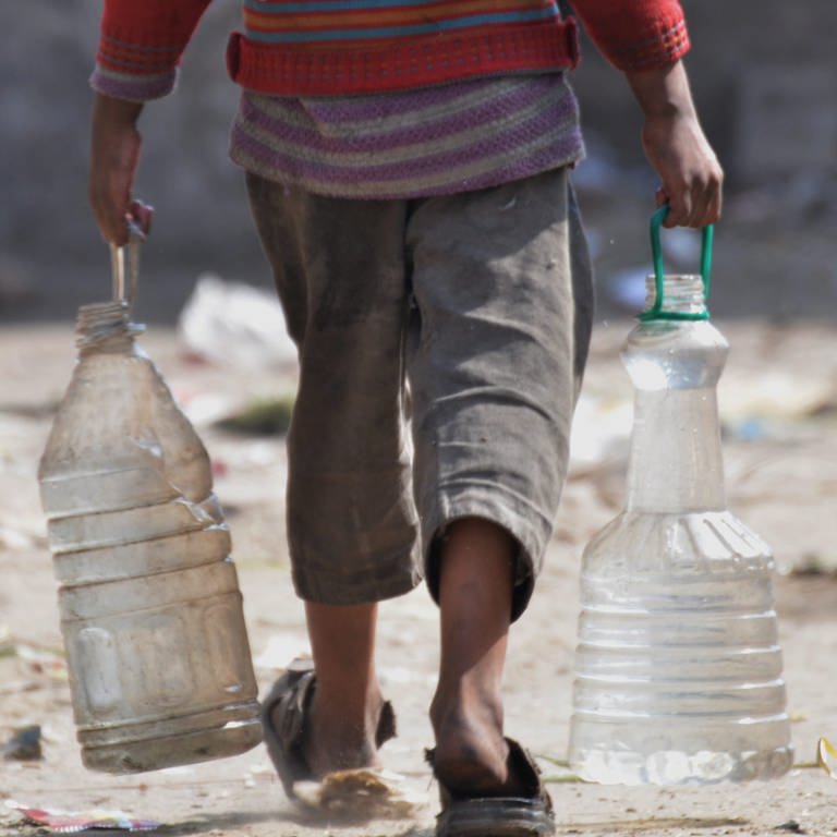 Ein Mann trägt in beiden Händen große FlaschenKanister voller Wasser.  (Foto: picture-alliance / Reportdienste, picture alliance / Pacific Press | Rana Sajid Hussain)