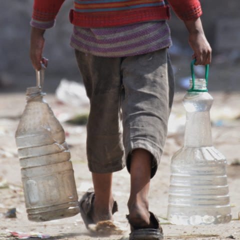 Ein Mann trägt in beiden Händen große FlaschenKanister voller Wasser. 