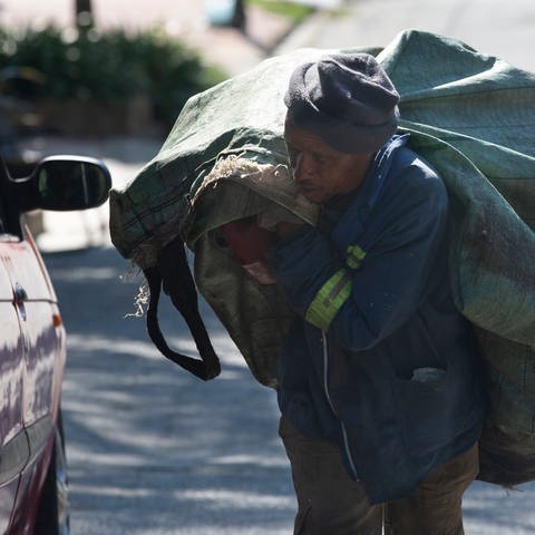 Ein Müllsammler trägt seine Ladung zu seinem Sammelwagen in einem Vorort von Johannesburg