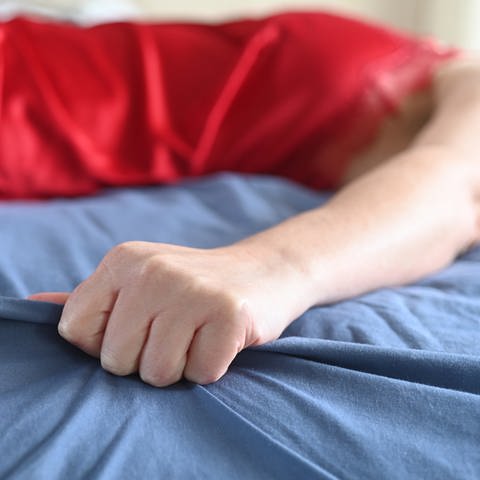 Frau hat einen Orgasmus im Bett. Nahaufnahme einer Hand, die das Laken ergreift. 