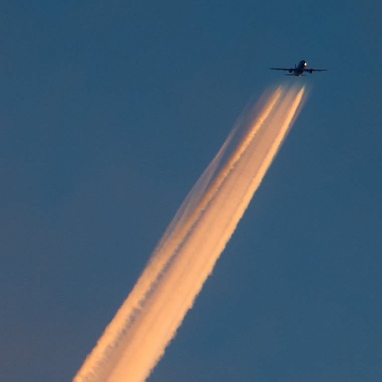 Die Triebwerksabgase von einem Flugzeug bilden einen von der untergehenden Sonne angestrahlten Kondensstreifen am Himmel 