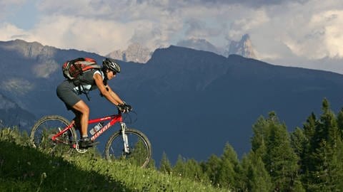 Mountainbike-Fahrer vor Gebirgslandschaft: Und Action! – Stress versorgt den Körper mit neuer Energie. Er macht uns wach und bereit, voll durchzustarten. Davon profitieren wir zum Beispiel beim Sport.