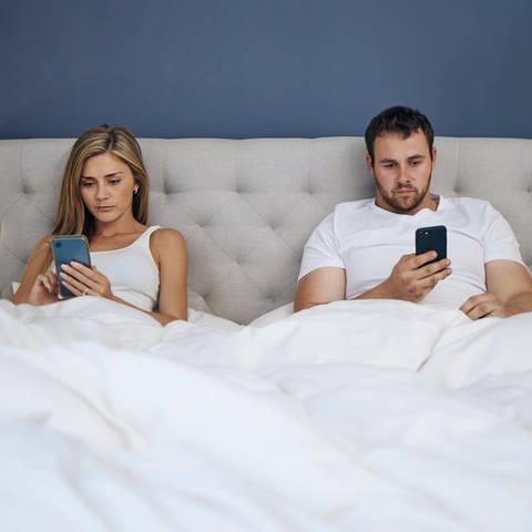 Ein junges Pärchen sitzt mit Handys im Bett
