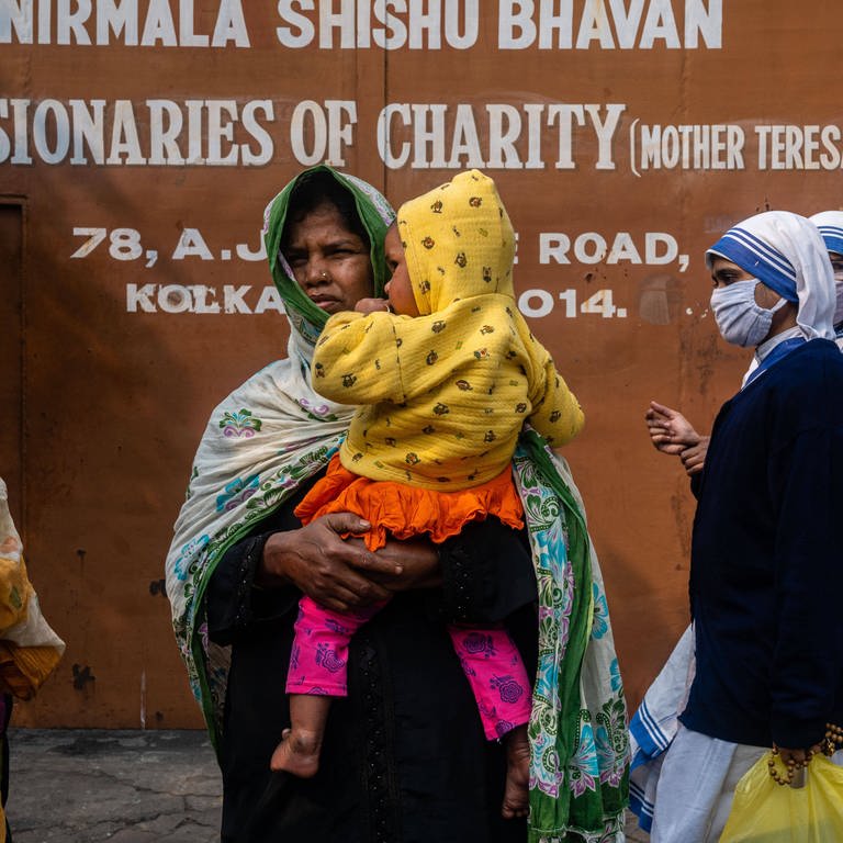 Patienten, die zu einer Gesundheitsuntersuchung bei den "Missionaries of Charity" in Kalkutta, gekommen sind, warten im Dezember 2021 vor dem Tor, während zwei Schwestern an ihnen vorbeigehen. Indiens hindu-nationalistische Regierung schneidet immer mehr christliche, muslimische und andere nicht genehme Hilfsorganisationen von ausländischer Finanzhilfe ab. Seit 2015 haben fast 20.000 NGOs die erforderliche Lizenz verloren.