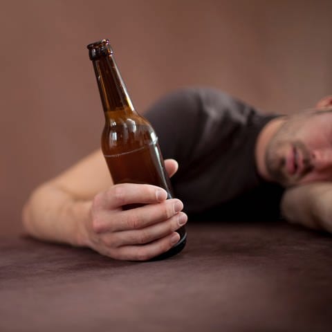Ein Mann liegt mit dem Oberkörper an der Tischkante und hält eine Flasche Bier in der Hand (Foto: picture-alliance / Reportdienste, picture alliance / photothek | Ute Grabowsky)