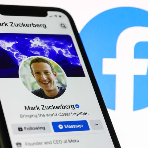 Das Facebook-Profil von Mark Zuckerberg, das auf einem Telefonbildschirm angezeigt wird, und das Facebook-Logo, das auf einem Bildschirm im Hintergrund angezeigt wird, sind auf diesem Illustrationsfoto zu sehen (Foto: IMAGO, IMAGO / NurPhoto)