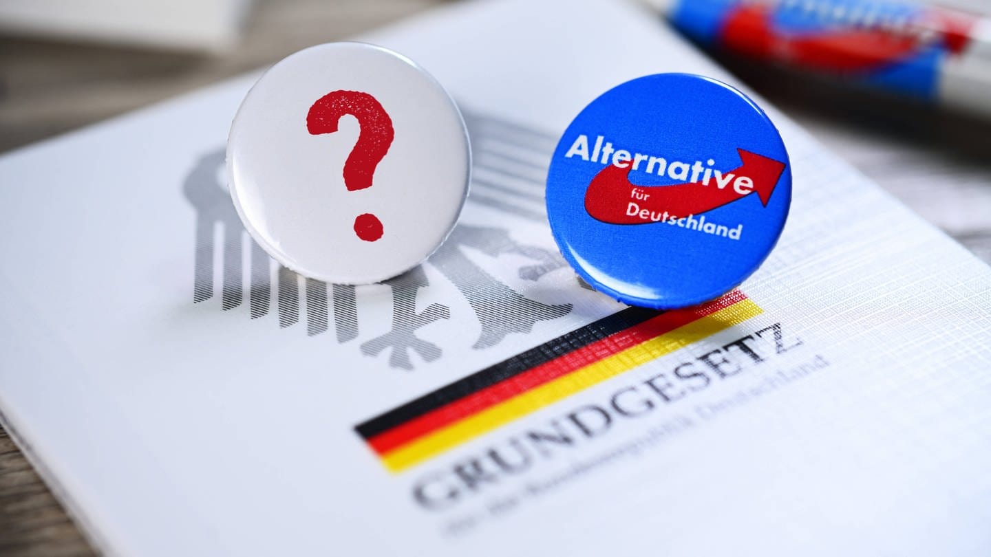 Parteianstecker der AfD und ein Fragezeichen liegen auf dem deutschen Grundgesetz: Eine politische Partei zu verbieten, ist laut Bundesverfassungsgericht 