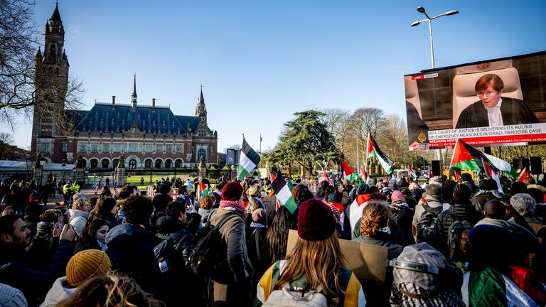 Demonstranten mit Flaggen Palästinas verfolgen auf einem Großbildschirm eine Übertragung aus dem Gericht: Demonstration in Den Haag vor dem Friedenspalast. Der Internationale Gerichtshof (IGH) prüft Südafrikas Vorwurf des Völkemords gegenüber Israel. Eine endgültige Entscheidung kann Jahre dauern, aber einstweilige Maßnahmen können bereits verhängt werden.