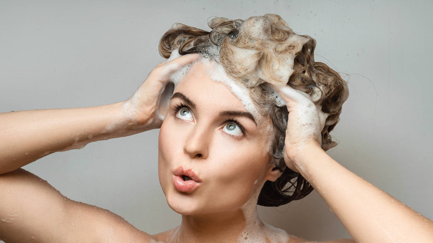 IMAGO / Zoonar (Foto: IMAGO, Junge Frau wäscht sich die Haare: Bio ist bei Naturkosmetik nicht so klar geregelt wie bei Lebensmitteln. Neben Zusatzstoffen ist beim Shampoo auch die Energiebilanz wichtig.)