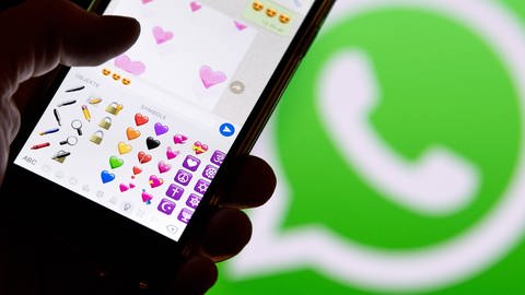 Ein Smartphone mit Emojis aus WhatsApp vor dem WhatsApp-Logo (Foto: picture-alliance / Reportdienste, picture alliance / Fabian Sommer/dpa | Fabian Sommer)