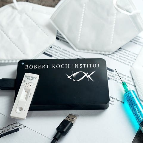Symbolbild RKI-Protokolle zu Covid-19. Eine Festplatte mit dem RKI (Robert-Koch-Institut) Logo liegt auf geschwärzten Dokumenten zusammen mit FFP2-Masken, Spritze und Schnelltest. FOTOMONTAGE