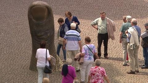 Menschen beschauen eine Bronze eines gigantischen Daumens. (Foto: SWR, SWR -)