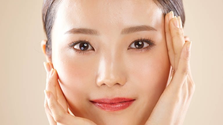 Gesicht einer hübschen jungen asiatischen Frau: Attraktive Menschen scheinen es im Leben leichter zu haben. Studien weisen darauf hin, dass sie eher positive Aufmerksamkeit bekommen und mehr Karrierechancen im Beruf haben. 