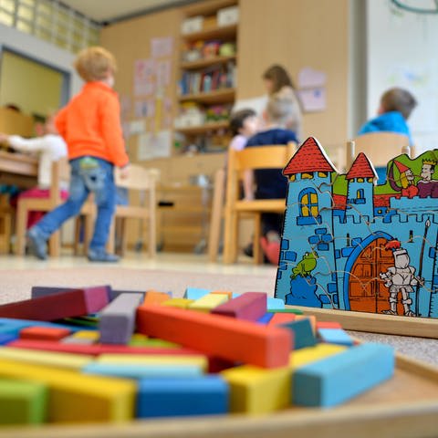 Spielzeug liegt in einer Kindertagesstätte auf dem Boden; im Hintergrund spielende Kinder: Knapp ein Prozent aller Kinder und Jugendlichen in Deutschland leben mit verschiedenen Ausprägungen von Autismus. Das fordert viele Kindergärten und Schulen besonders heraus.