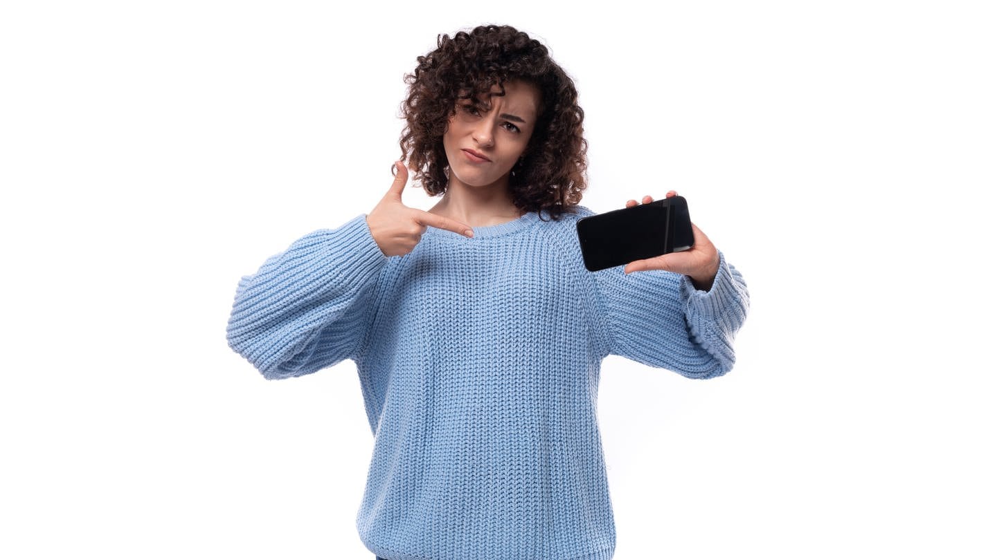 Eine junge Dame mit schwarzen Locken und einem hellblauen Pullover zeigt den Bildschirm auf einem Handy. (Foto: IMAGO, IMAGO / Pond5 Images)