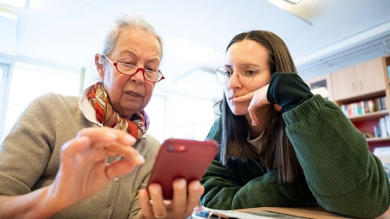Smartphone-Sprechstunde für Senioren: Eine junge Frau erklärt einer älteren Funktionen am Handy. Seit Jahrzehnten labeln Gesellschaften Alterskohorten in bestimmte "Generationen", die vermeintlich Erfahrungen und Verhalten miteinander teilen. Doch was ist dran an Zuschreibungen wie Boomer, Millenials oder Gen Z?