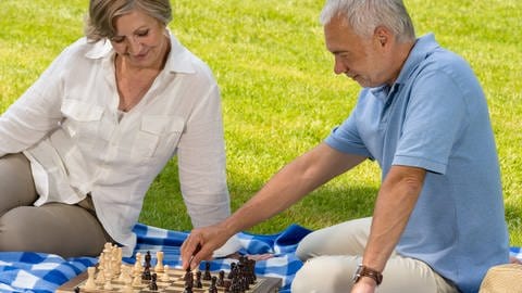 Zwei ältere Menschen spielen Schach auf einer Picknickdecke.