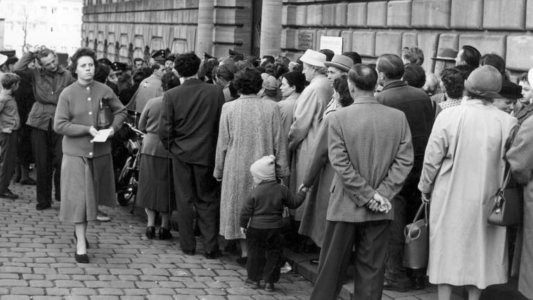 Menschen stehen am 18.10.1957 vor der Ortskrankenkasse in Nürnberg Schlange. Der Andrang war so groß, dass die Nürnberger Stadtpolizei zur Hilfeleistung herangezogen wurde.