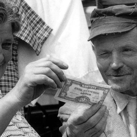 Ein Ehepaar vergleicht am 6. Juli 1959 auf dem Saarbrücker Markt alte und neue Geldscheine (Foto: picture-alliance / dpa, picture-alliance / dpa -)