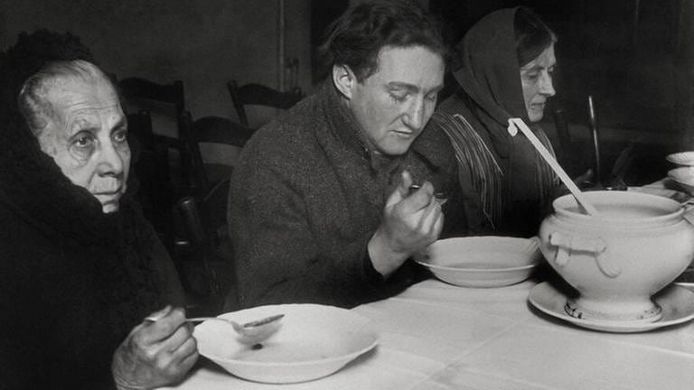 Speisung von Arbeitslosen und Bedürftigen aus privaten Mitteln in einer Wärmehalle in Berlin-Neukölln im Januar 1931. Auch im Reichstag wird das wachsende Elend in der Bevölkerung diskutiert.