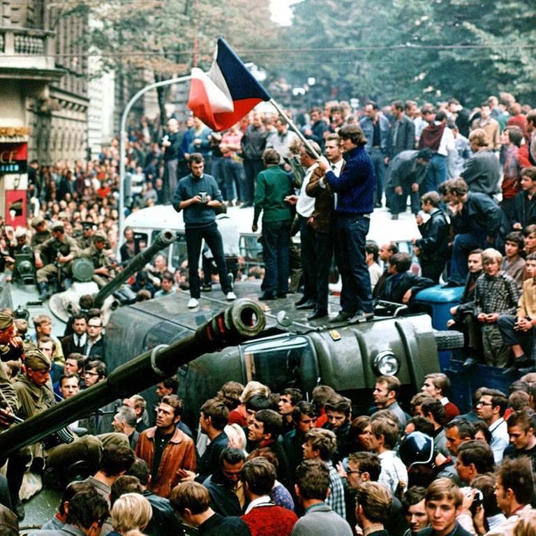 Demonstranten protestieren und umringen in der Prager Innenstadt sowjetische Panzer. Einige stehen mit einer Fahne der Tschechoslowakei auf einem umgekippten Militärfahrzeug
