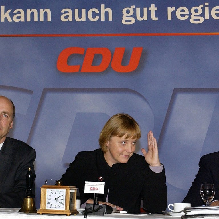 Die Bundesvorsitzende der CDU, Angela Merkel, sitzt am 11.1.2002 während einer zweitägigen Klausur-Tagung ihrer Partei in Magdeburg zwischen CDU-Generalsekretär Lorenz Meyer (links) und dem Vorsitzenden der nordrhein-westfälischen CDU, Jürgen Rüttgers. (Foto: picture-alliance / Reportdienste, picture-alliance / dpa | Bernd Settnik)